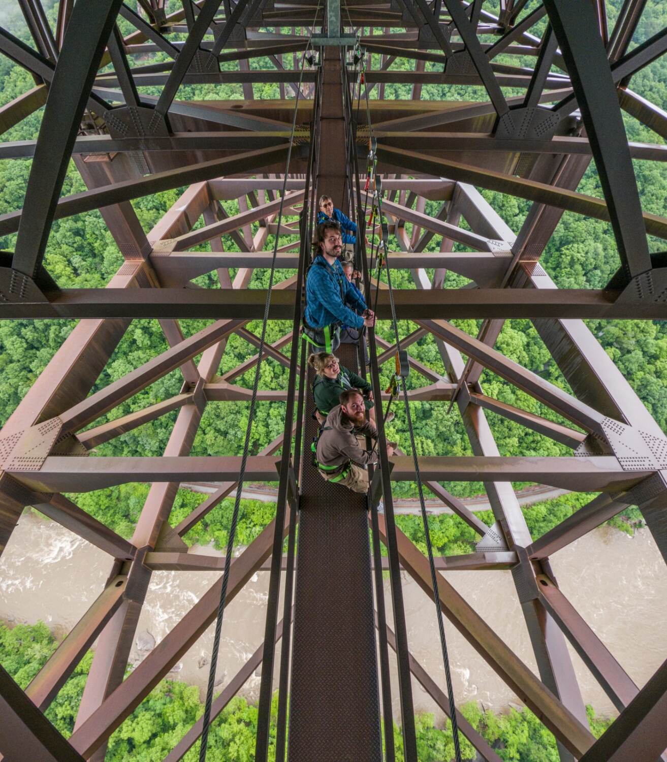 View looking up through the New River Gorge Bridge steel structure with Bridge Walk guests on the catwalk